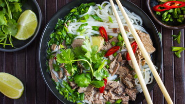beef pho on wooden background with limes and cilantro